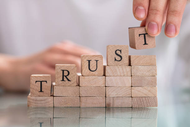 Woman's Hand Placing Last Alphabet Of Word Trust Over Wooden Block